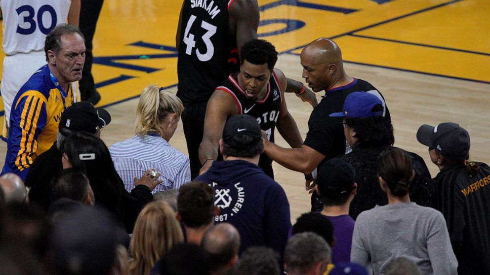 Toronto Raptors guard Kyle Lowry, middle, gestures next to referee Marc Davis (8) near the front row of fans during the second half of Game 3 of basketball's NBA Finals between the Golden State Warriors and the Raptors in Oakland, Calif., Wednesday, 