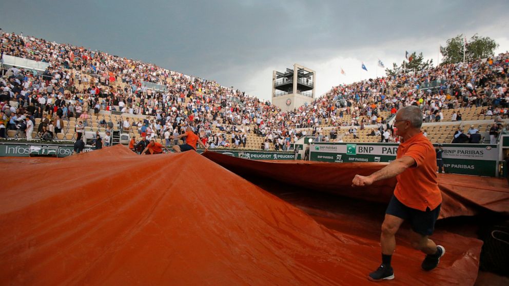 Workers cover Suzanne Lenglen court because of rain during the quarterfinal match of the French Open tennis tournament between Switzerland's Stan Wawrinka and Switzerland's Roger Federer at the Roland Garros stadium in Paris, Tuesday, June 4, 2019. (