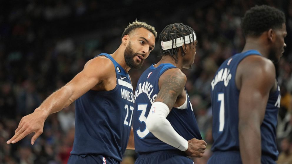 Minnesota Timberwolves center Rudy Gobert (27), left, speaks with forward Jaden McDaniels (3), middle, during the first half of an NBA basketball game against the Milwaukee Bucks, Friday, Nov. 4, 2022, in Minneapolis. (AP Photo/Abbie Parr)