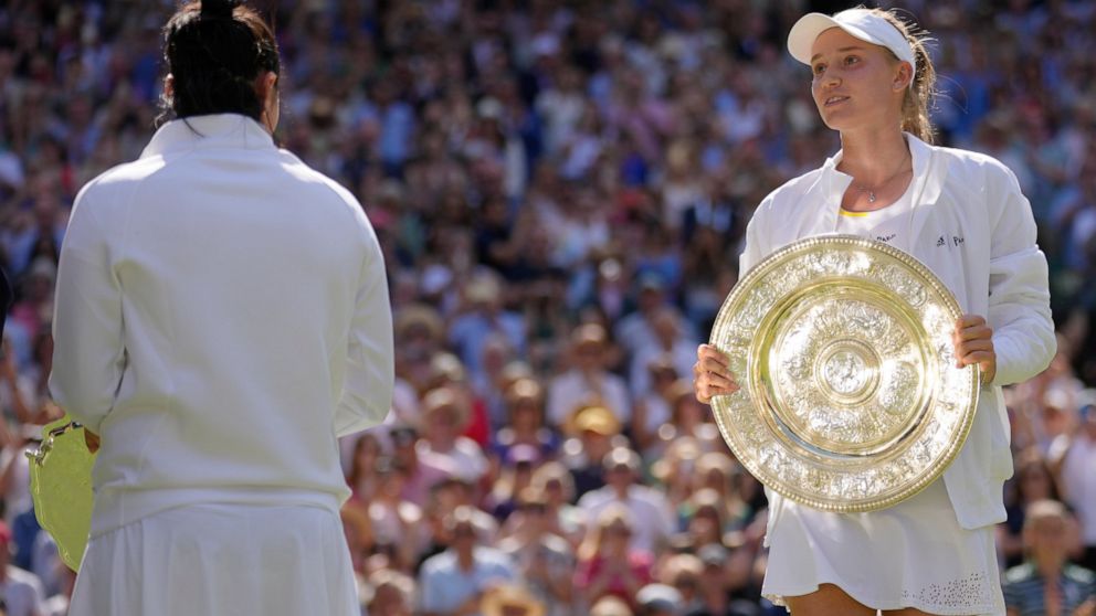 Kazakhstan's Elena Rybakina celebrates with the trophy after beating Tunisia's Ons Jabeur, left, to win the final of the women's singles on day thirteen of the Wimbledon tennis championships in London, Saturday, July 9, 2022. (AP Photo/Kirsty Wiggles