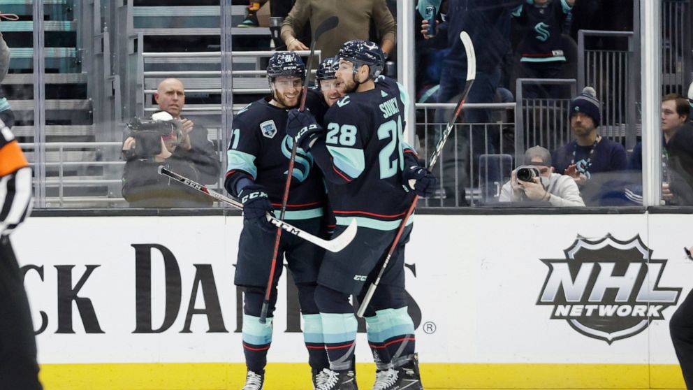 Seattle Kraken center Alex Wennberg, left and defenseman Carson Soucy (28) embrace left wing Jared McCann after he scored against the Dallas Stars during the first period of an NHL hockey game Sunday, April 3, 2022, in Seattle. (AP Photo/John Froschauer)