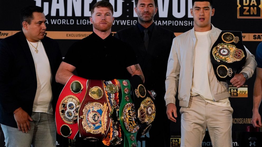 Canelo Alvarez, second from left, of Mexico, poses with Dmitry Bivol, right, of Russia, Wednesday, March 2, 2022, in San Diego as promoter Eddie Hearn, second from right, and Alvarez's trainer, Eddy Reynoso, left, look on. Alvarez is scheduled to fig