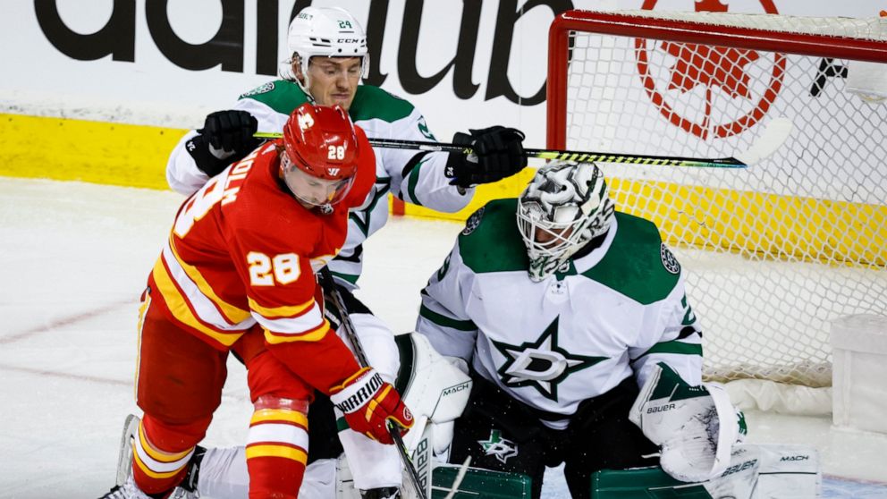 Dallas Stars goalie Jake Oettinger, right, defends as Calgary Flames center Elias Lindholm, front left, tries to score while being checked by Stars center Roope Hintz during the second period of Game 1 of an NHL hockey first-round playoff series Tues