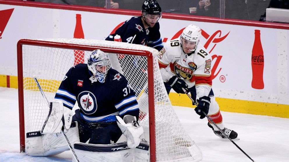 Florida Panthers' Matthew Tkachuk (19) carries the puck behind Winnipeg Jets goaltender Connor Hellebuyck (37) during the first period of an NHL hockey game Tuesday, Dec. 6, 2022, in Winnipeg, Manitoba. (Fred Greenslade/The Canadian Press via AP)