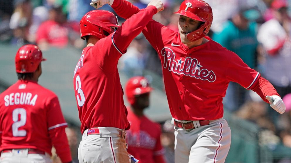 Philadelphia Phillies' Rhys Hoskins, right, is greeted by Bryce Harper, center, at the plate after Hoskins hit a grand slam against the Seattle Mariners to score Harper during the fourth inning of a baseball game, Wednesday, May 11, 2022, in Seattle.