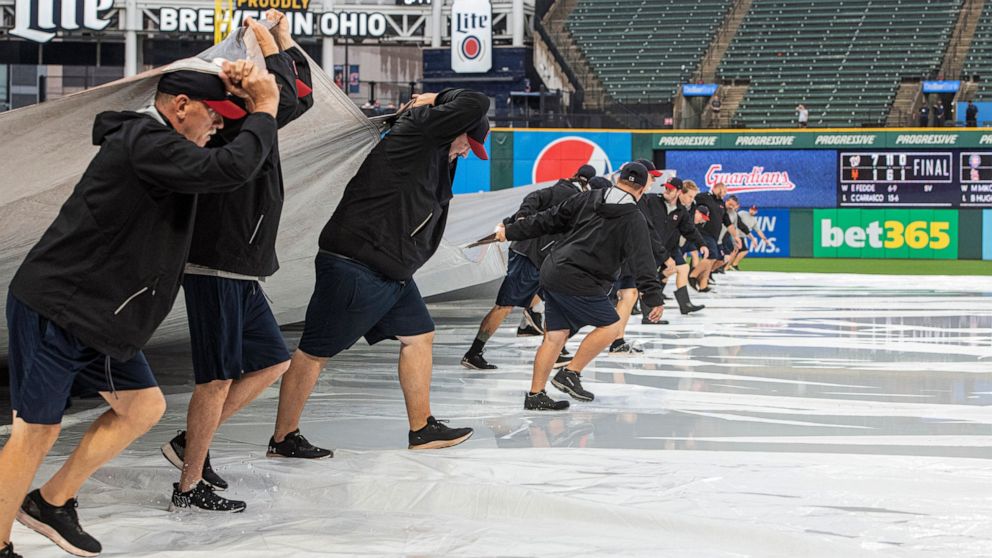 Members of the Cleveland Guardians grounds crew remove the tarp from the infield as they attempt to get the field ready to play during the fourth inning of a baseball game between the Seattle Mariners and the Guardians in Cleveland, Sunday, Sept. 4, 