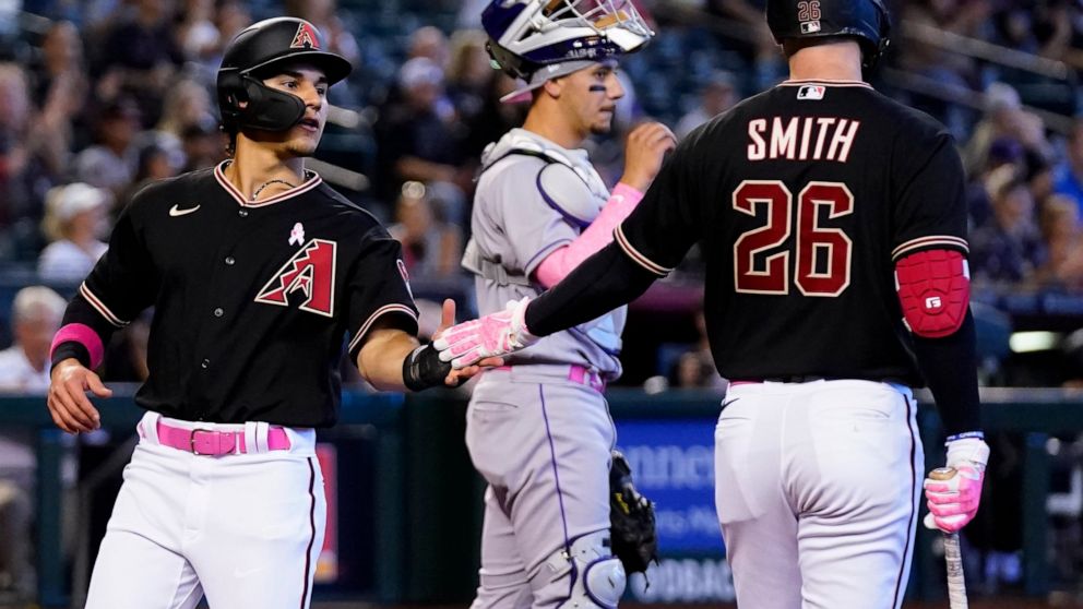 Arizona Diamondbacks' Alek Thomas, left, celebrates with teammate Pavin Smith (26) after scoring as Colorado Rockies catcher Dom Nunez, center, pauses at home plate in the fifth inning of a baseball game Sunday, May 8, 2022, in Phoenix. (AP Photo/Ros