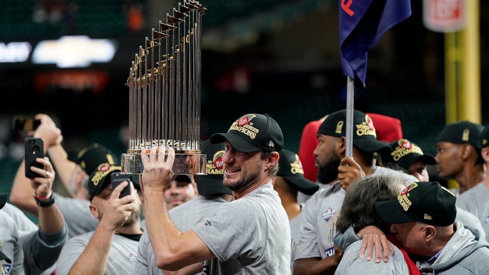 FILE - In this Oct. 30, 2019, file photo, Washington Nationals starting pitcher Max Scherzer celebrates with the trophy after Game 7 of the baseball World Series against the Houston Astros in Houston. The Nationals head to spring training with mostly