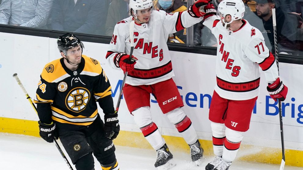 Carolina Hurricanes center Seth Jarvis, center, is congratulated by Tony DeAngelo (77) after his goal as Boston Bruins left wing Jake DeBrusk, left, skates past during the first period of an NHL hockey game, Tuesday, Jan. 18, 2022, in Boston. (AP Pho