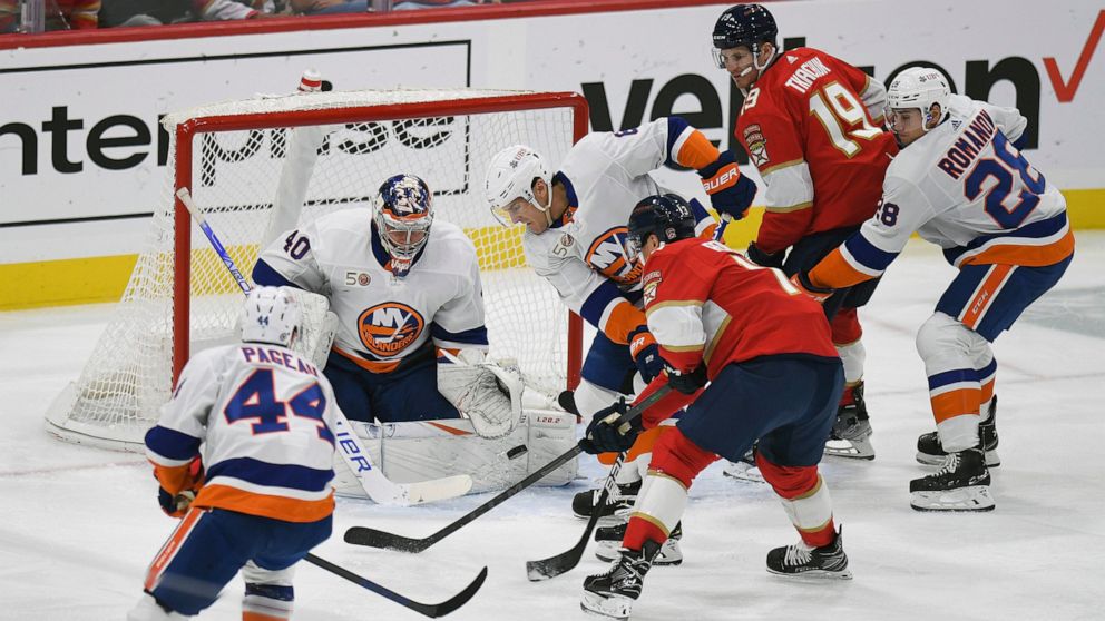 New York Islanders' Ryan Pulock, center, stops the puck in front of Florida Panthers' Sam Reinhart during the first period of an NHL hockey game, Sunday, Oct. 23, 2022, in Sunrise, Fla. (AP Photo/Michael Laughlin)