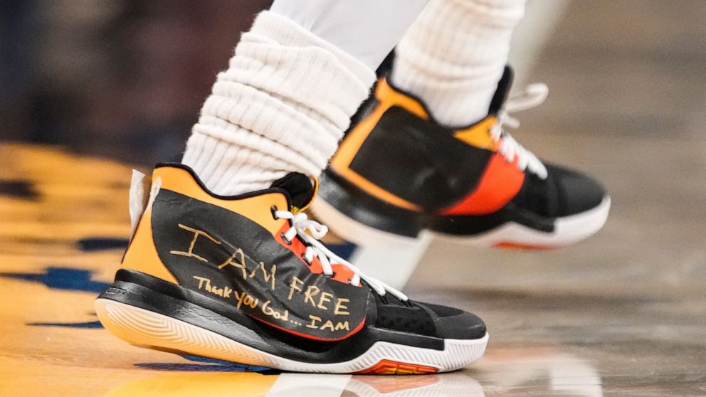 Brooklyn Nets guard Kyrie Irving (11) wears sneakers with logos covered in tape with the words "I AM FREE Thank you God … I AM" written in gold colored marker during the second half of an NBA basketball game against the Charlotte Hornets, Wednesday, 