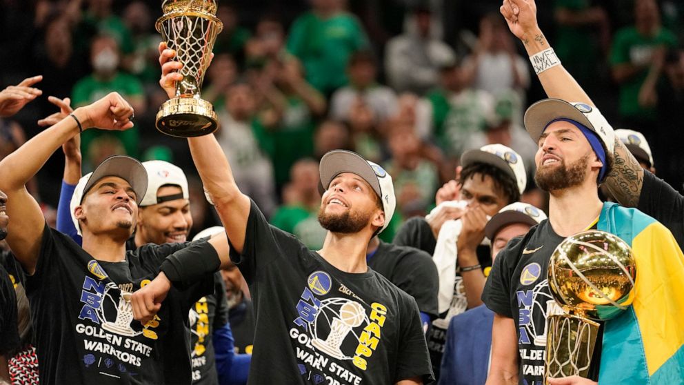 Golden State Warriors guard Stephen Curry, center, holds up the Bill Russell Trophy for most valuable player after the Warriors defeated the Boston Celtics in Game 6 to win basketball's NBA Finals championship, Thursday, June 16, 2022, in Boston. (AP