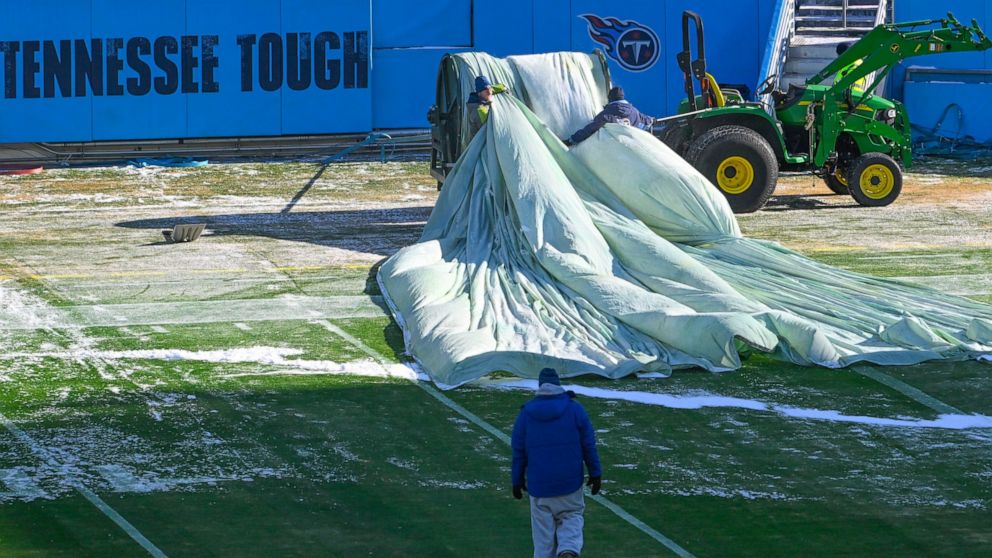 Crews remove tarps that covered the field overnight before an NFL football game between the Tennessee Titans and the Houston Texans, Saturday, Dec. 24, 2022, in Nashville, Tenn. Extreme cold weather has hit the region. (AP Photo/John Amis)