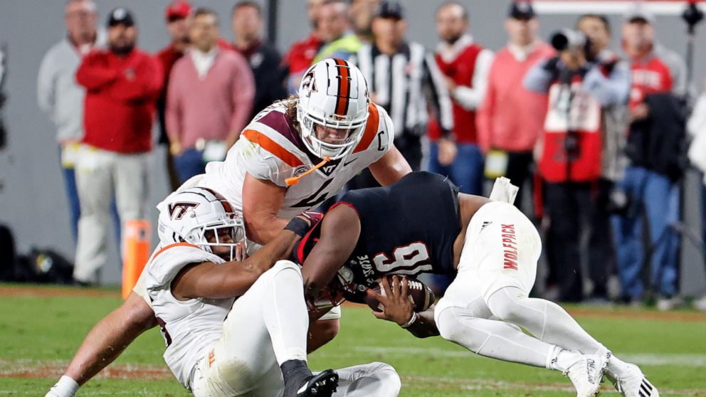 North Carolina State quarterback MJ Morris (16) is tackled by Virginia Tech's TyJuan Garbutt, left, and Dax Hollifield (4) during the first half of an NCAA college football game in Raleigh, N.C., Thursday, Oct. 27, 2022. (AP Photo/Karl B DeBlaker)