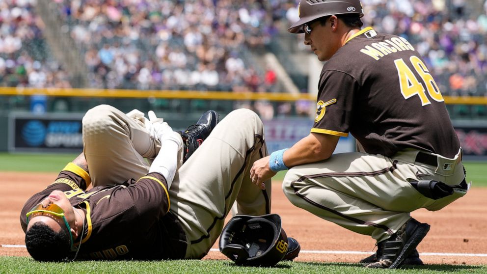 San Diego Padres first base coach David Macias, right, looks to help Manny Machado after Machado was injured while trying to run out an infield hit to Colorado Rockies starting pitcher Antonio Senzatela in the first inning of a baseball game Sunday, 