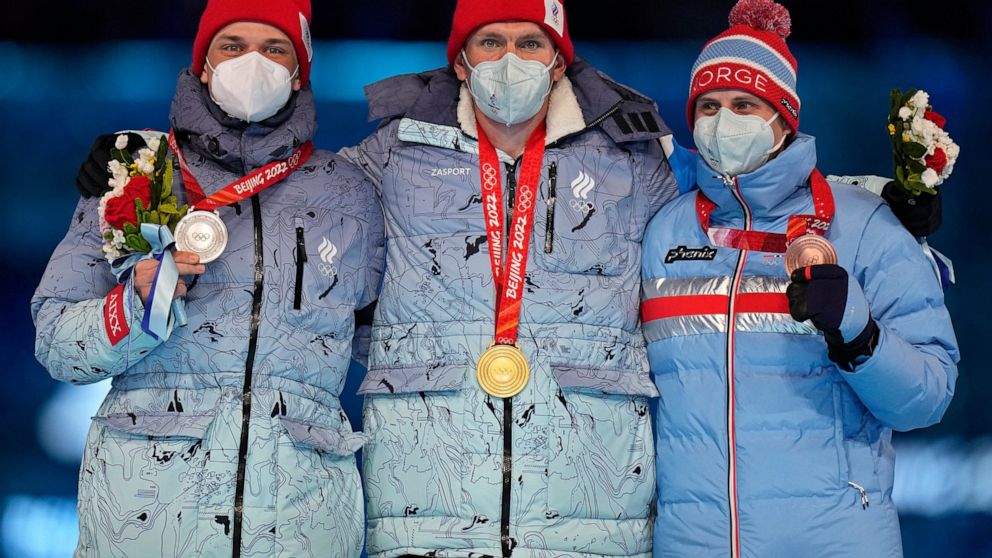 Gold medalist for the men's weather-shortened 50km mass start free cross-country skiing competition, Alexander Bolshunov, centre, of the Russian Olympic Committee stands with compatriot and silver medalist, Ivan Yakimushkin, left, and bronze medalist