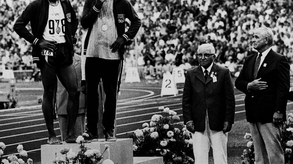 FILE - U.S. runners Wayne Collett (978) and Vince Matthews stand at ease on the top level of the victory stand Sept. 7, 1972, at Olympic Stadium in Munich. The International Olympic Committee banned the two from further competition although Matthews 