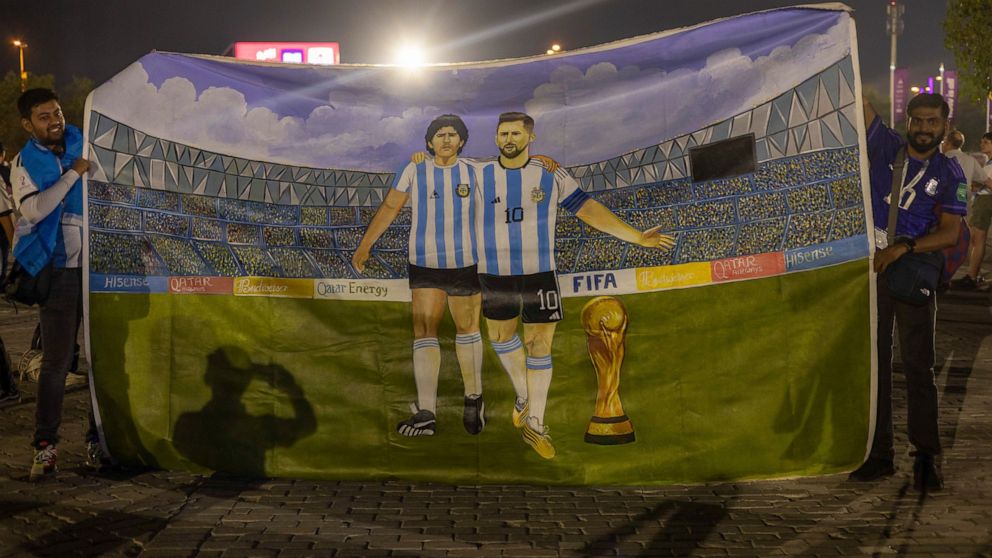 Mohid Data and Aayush Verma from India show a huge painting of their heroes, Lionel Messi and Diego Maradona with the World Cup trophy, prior to the World Cup group C soccer match between Poland and Argentina at the Stadium 974 in Doha, Qatar, Wednes