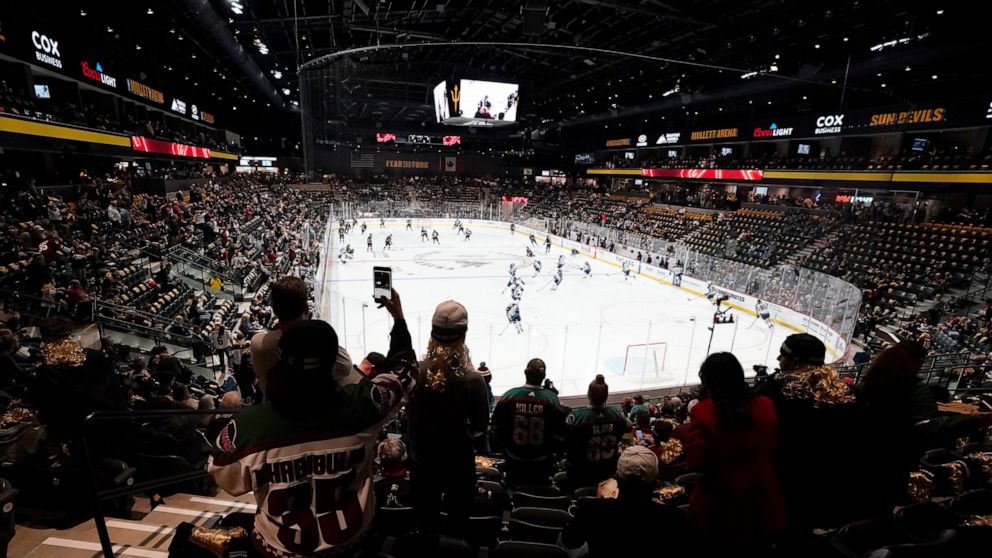 Fans watch players as they warm up prior to the Arizona Coyotes NHL home-opening hockey game against the Winnipeg Jets at the 5,000-seat Mullett Arena in Tempe, Ariz., Friday, Oct. 28, 2022. The Coyotes will share the arena with the Arizona State NCA