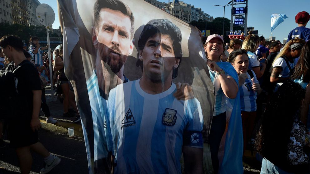 A flag featuring Lionel Messi, left, and the late soccer great Maradona hangs amid Argentina soccer fans after they watched the team's World Cup semifinal win over Croatia, hosted by Qatar, on a screen set up in the Palermo neighborhood of Buenos Air