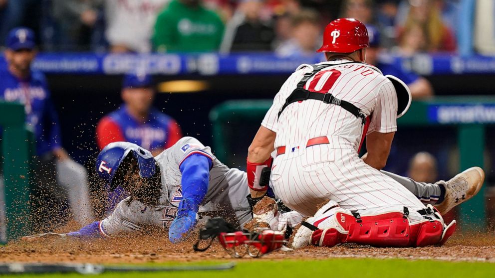 Texas Rangers' Adolis Garcia, left, is tagged out at home by Philadelphia Phillies catcher J.T. Realmuto after trying to score on a fly out by Zach Reks during the seventh inning of a baseball game, Wednesday, May 4, 2022, in Philadelphia. (AP Photo/