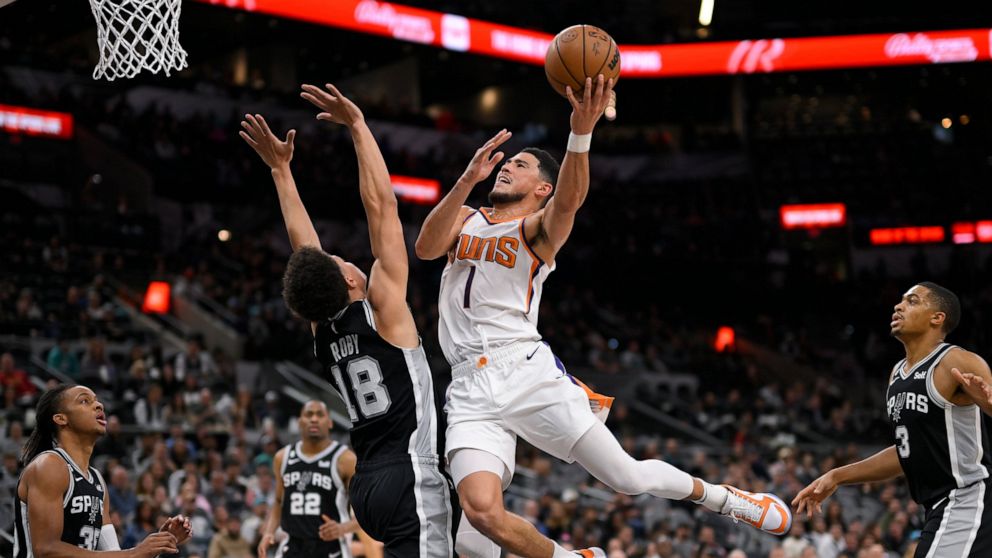 Phoenix Suns' Devin Booker (1) shoots against San Antonio Spurs' Isaiah Roby during the first half of an NBA basketball game, Sunday, Dec. 4, 2022, in San Antonio. (AP Photo/Darren Abate)