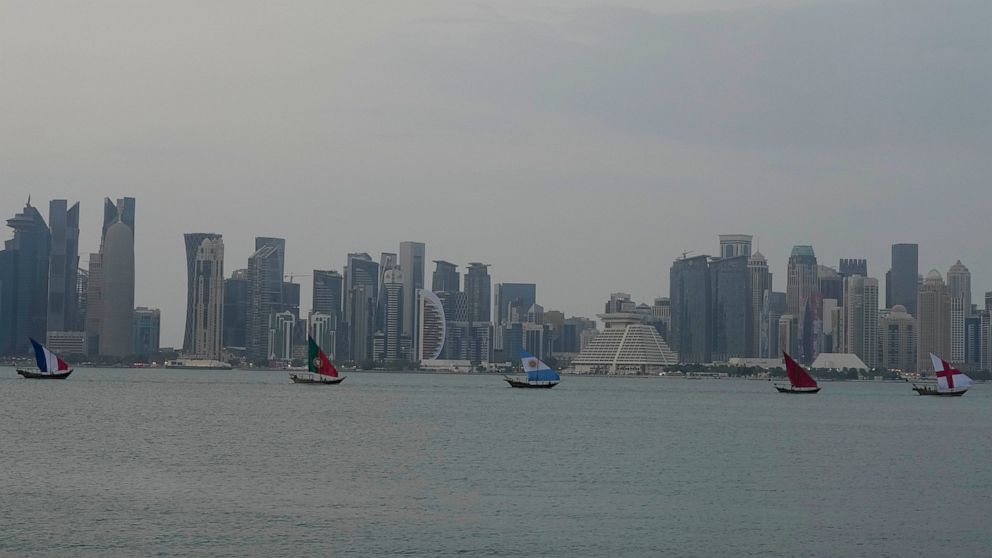 Boats with flags of quarterfinal participating countries pass the skyline of Doha, Qatar, on Wednesday, Dec. 7, 2022. (AP Photo/Frank Augstein)