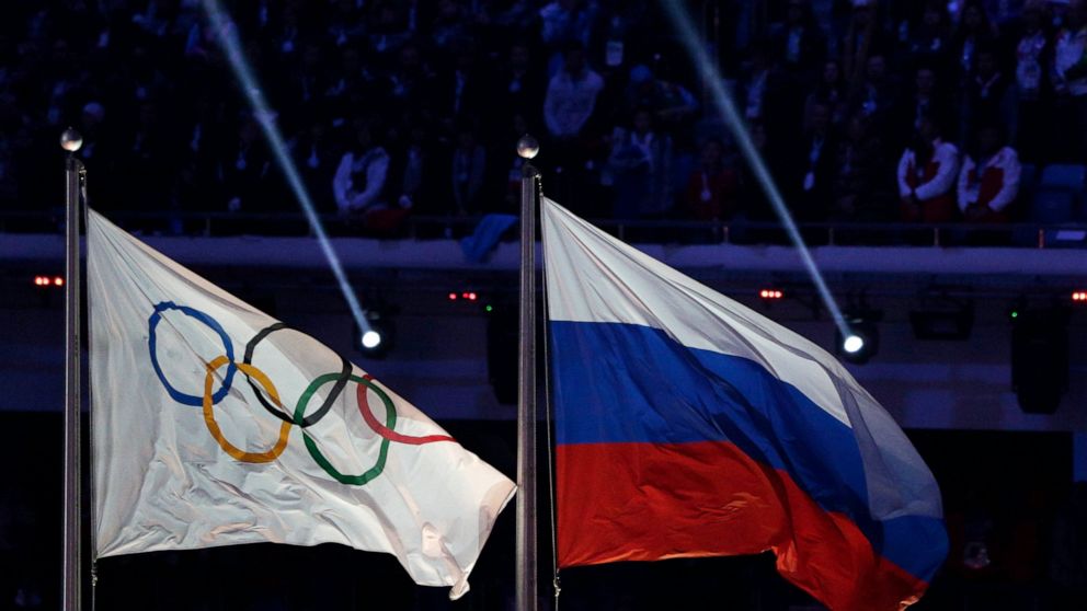 FILE - In this Feb. 23, 2014 file photo, the Russian national flag, right, flies after next to the Olympic flag during the closing ceremony of the 2014 Winter Olympics in Sochi, Russia. The World Anti-Doping Agency banned Russia on Monday Dec. 9, 201