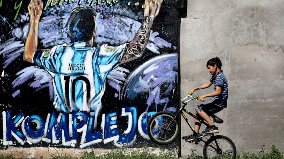In this Dec. 5, 2019 photo, a boys pops a wheelie as he rides his bicycle past a mural featuring Lionel Messi in La Bajada, Rosario, Argentina. Soccer wasn't always Messi's favorite activity. When he was a child in the modest neighborhood of La Bajad