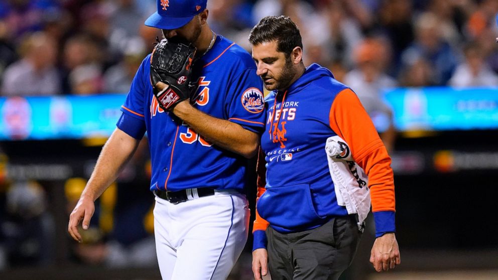 New York Mets starting pitcher Tylor Megill, left, talks to a trainer as he leaves during the fourth inning of the team's baseball game against the Milwaukee Brewers on Thursday, June 16, 2022, in New York. (AP Photo/Frank Franklin II)