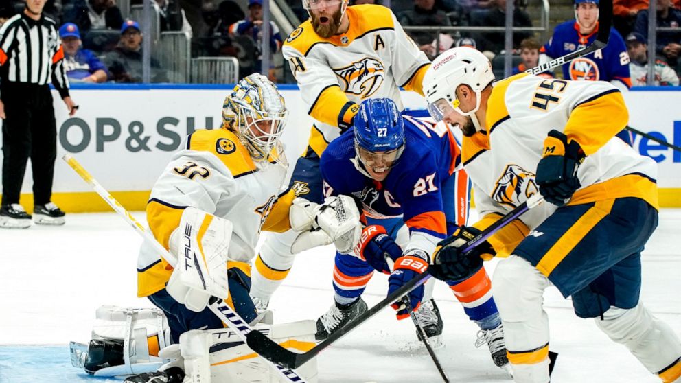 New York Islanders left wing Anders Lee (27) and Nashville Predators defenseman Alexandre Carrier (45) fight for the puck as Predators goaltender Kevin Lankinen (32) guards the goal during the second period of an NHL hockey game, Friday, Dec. 2, 2022