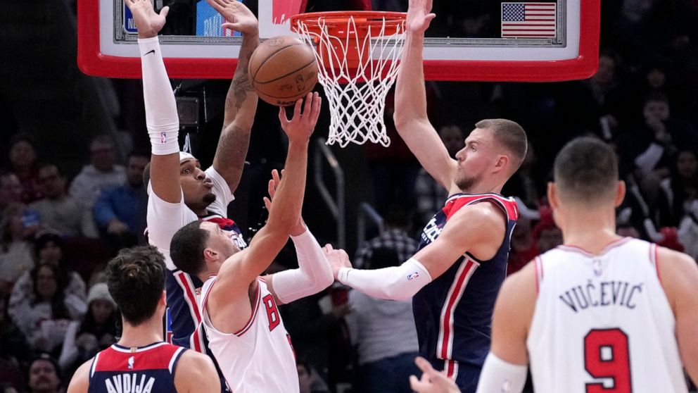Chicago Bulls' Zach LaVine shorts between Washington Wizards' Daniel Gafford, left, and Kristaps Porzingis during the second half of an NBA basketball game Wednesday, Dec. 7, 2022, in Chicago. The Bulls won 115-111. (AP Photo/Charles Rex Arbogast)