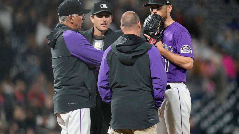 Colorado Rockies starting pitcher Chad Kuhl, right, confers with trainer Heath Townsend, second from right, home plate umpire Pat Hoberg, second from left, and manager Bud Black, left, as Kuhl is pulled from the mound before facing a Philadelphia Phi