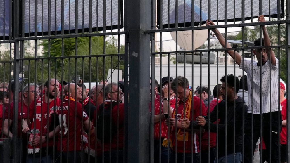 A fan climbs on the fence in front of the Stade de France prior the Champions League final soccer match between Liverpool and Real Madrid, in Saint Denis near Paris, Saturday, May 28, 2022. Police have deployed tear gas on supporters waiting in long 