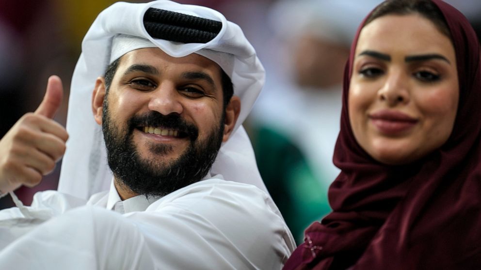 A couple on the tribune smiles to the camera prior the World Cup, group A soccer match between Qatar and Ecuador at the Al Bayt Stadium in Doha, Sunday, Nov. 20, 2022. (AP Photo/Natacha Pisarenko)