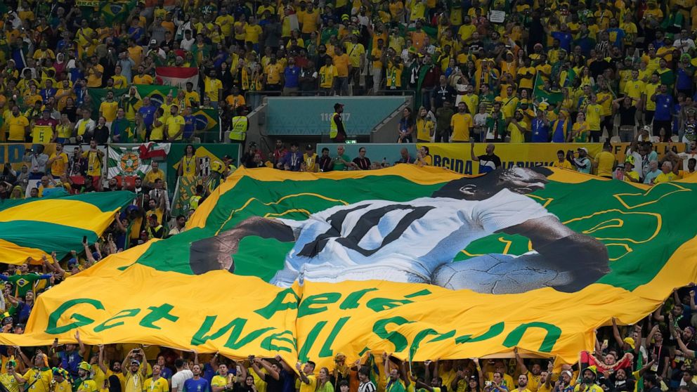 Brazilian fans hold a giant Brazilian flag with picture of former Brazilian player Pele with message reads in English "Pele, Get well soon," during the World Cup group G soccer match between Cameroon and Brazil, at the Lusail Stadium in Lusail, Qatar