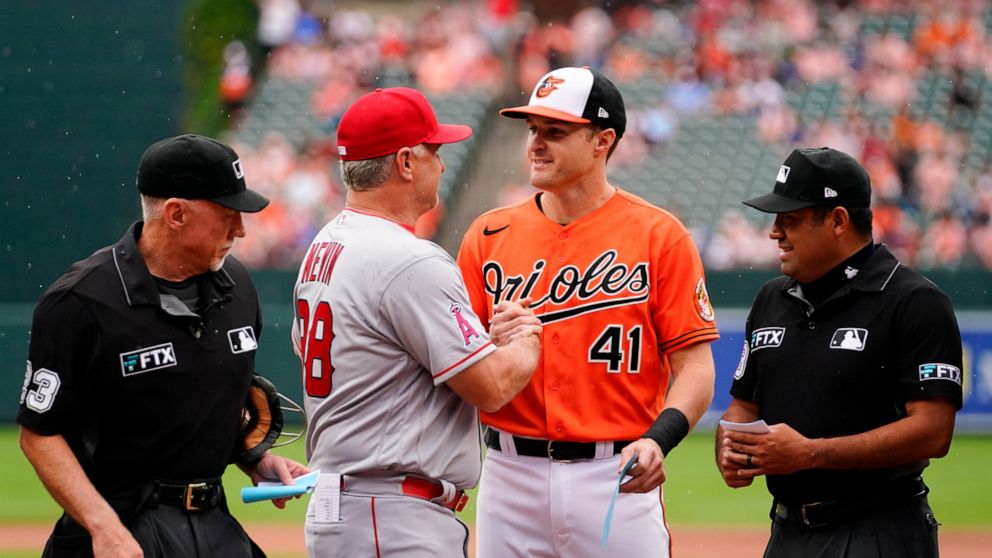 Los Angeles Angels interim manager Phil Nevin, center left, and his son, Baltimore Orioles third baseman Tyler Nevin, center right, shake hands after delivering their team's lineup cards as home plate umpire Lance Barksdale, left, and second base ump