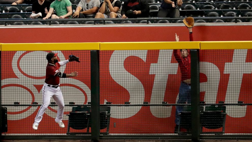 A fan tries to get a glove on a solo home run hit by Miami Marlins' Austin Dean during the fourth inning of a baseball game as Arizona Diamondbacks' Abraham Almonte looks on Wednesday, Sept. 18, 2019, in Phoenix. (AP Photo/Matt York)
