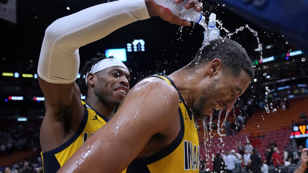 Indiana Pacers guard Buddy Hield, left, douses guard Tyrese Haliburton (0) after the team's NBA basketball game against the Miami Heat on Friday, Dec. 23, 2022, in Miami. Haliburton hit a 3-pointer with 2 seconds left. (AP Photo/Jim Rassol)