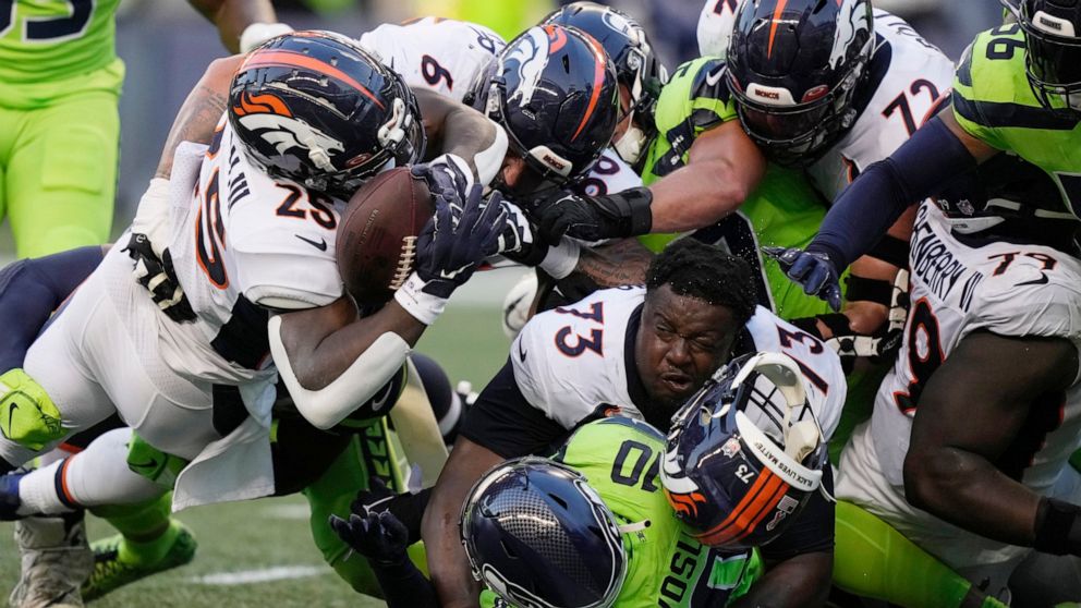 Denver Broncos running back Melvin Gordon III, upper left, fumbles the ball as Broncos offensive tackle Cameron Fleming (73) loses his helmet during the second half of an NFL football game against the Seattle Seahawks, Monday, Sept. 12, 2022, in Seat