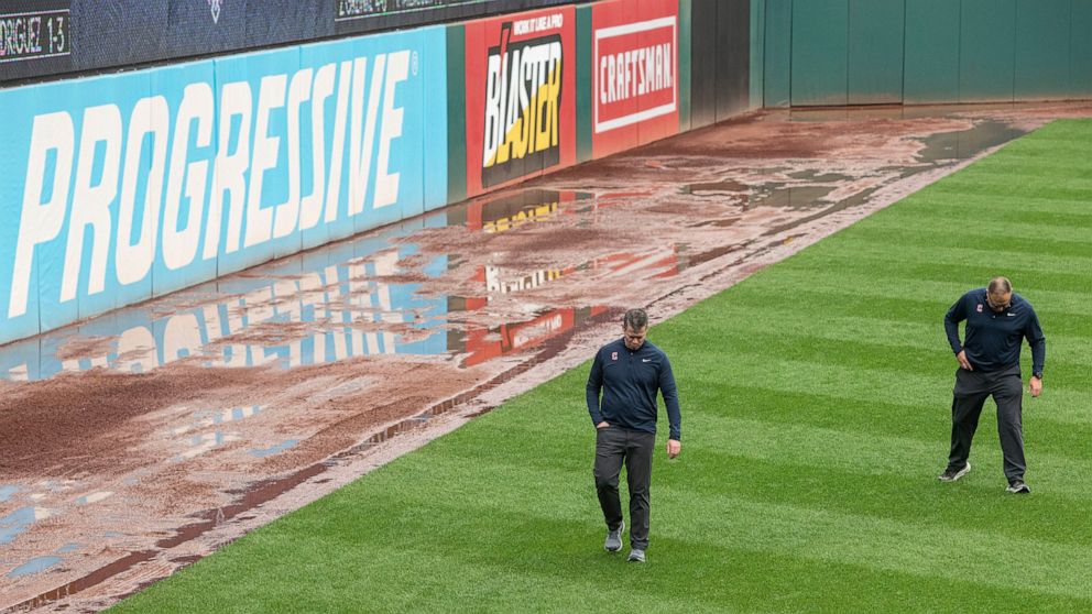 Members of the Cleveland Guardians ground crew inspect the left field turf at Progressive Field as water covers part of the warning track in left and center fields before a baseball game between the Chicago White Sox and the Guardians in Cleveland, S
