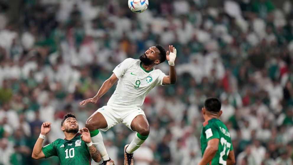 Mexico's Alexis Vega, left, and Mexico's Jesus Gallardo, right, watch Saudi Arabia's Firas Al-Buraikan jumping for the ball during the World Cup group C soccer match between Saudi Arabia and Mexico, at the Lusail Stadium in Lusail, Qatar, Wednesday, 