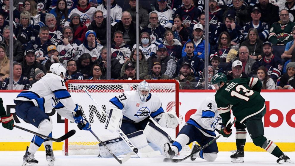Minnesota Wild's Sam Steel (13) takes a shot on Winnipeg Jets goaltender Connor Hellebuyck (37) during the second period of an NHL hockey game in Winnipeg, Manitoba, on Tuesday Dec. 27, 2022. (Fred Greenslade/The Canadian Press via AP)