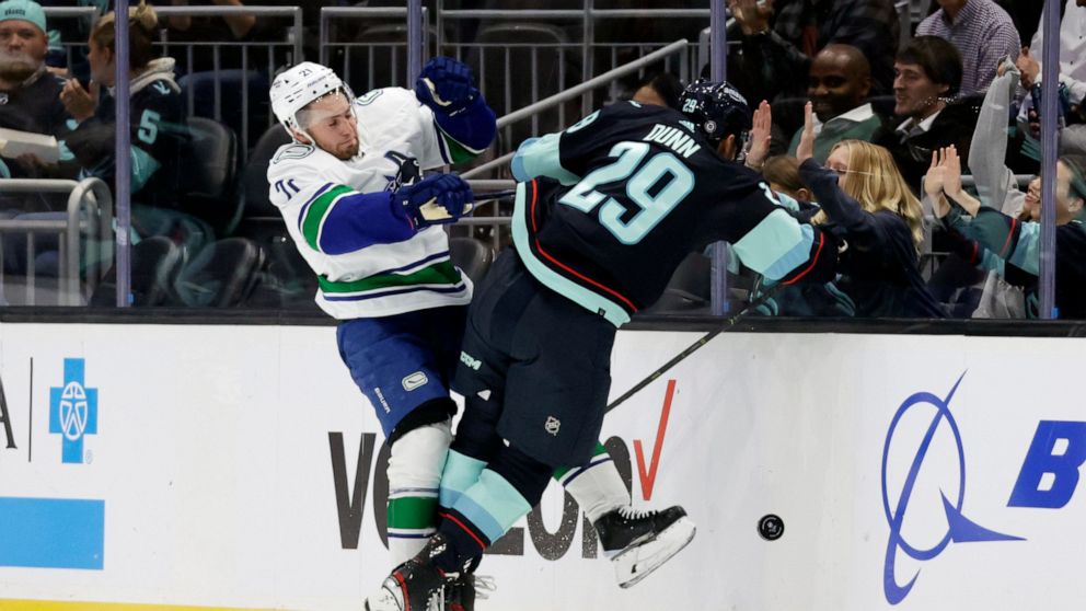 Vancouver Canucks left wing Nils Hoglander (21) collides with Seattle Kraken defenseman Vince Dunn (29) as they battle for the puck during the first period of an NHL hockey game, Thursday, Oct. 27, 2022, in Seattle. (AP Photo/John Froschauer)