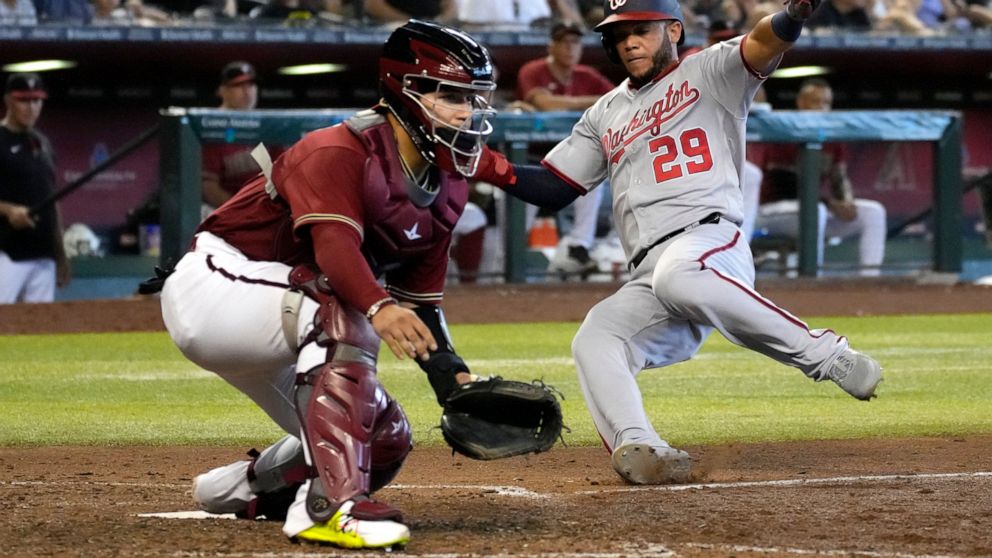 Washington Nationals' Yadiel Hernandez (29) scores against Arizona Diamondbacks catcher Jose Herrera, left, after a throwing error by third baseman Josh Rojas in the sixth inning during a baseball game, Sunday, July 24, 2022, in Phoenix. (AP Photo/Ri