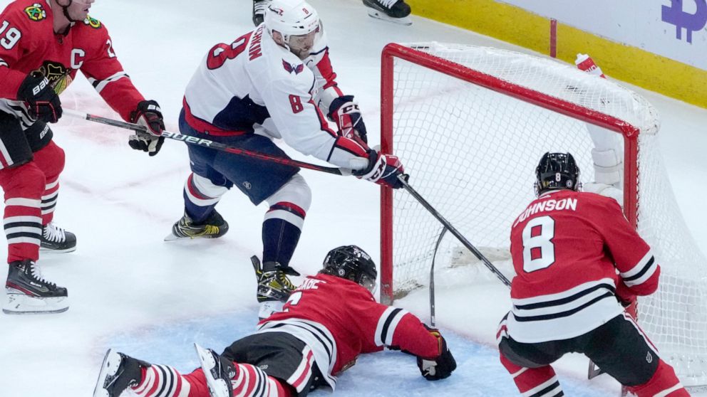 Washington Capitals' Alex Ovechkin scores his second goal of the game as Chicago Blackhawks' Jake McCabe and Jack Johnson (8) defend during the first period of an NHL hockey game Tuesday, Dec. 13, 2022, in Chicago. (AP Photo/Charles Rex Arbogast)