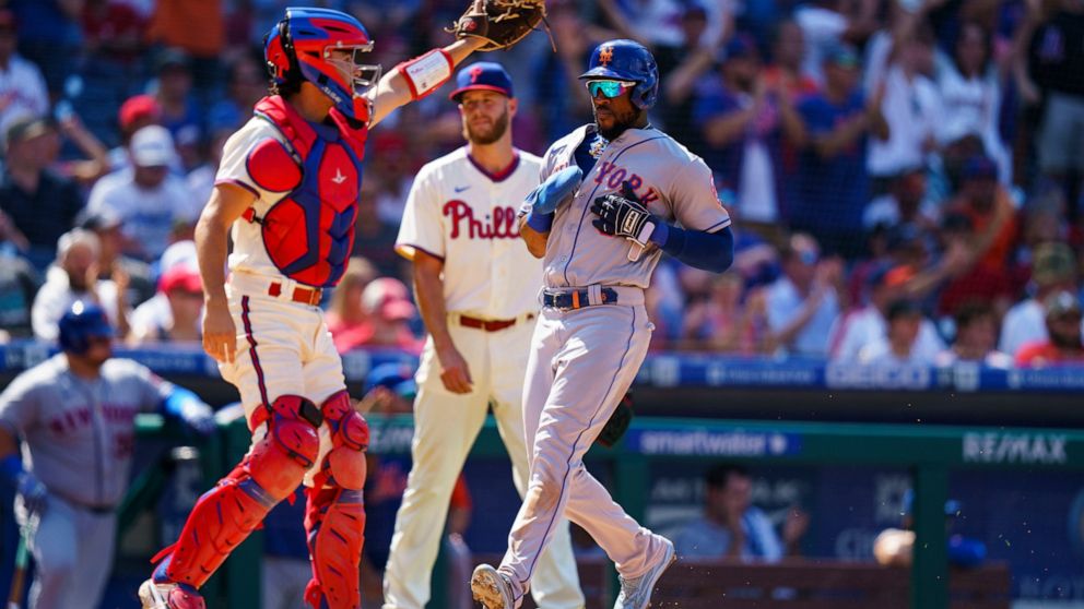 New York Mets' Starling Marte, right, comes in to score as Philadelphia Phillies catcher Garrett Stubbs, left, looks for the ball as starting pitcher Zack Wheeler, center, looks on during the first inning of the sixth baseball game of a doubleheader,