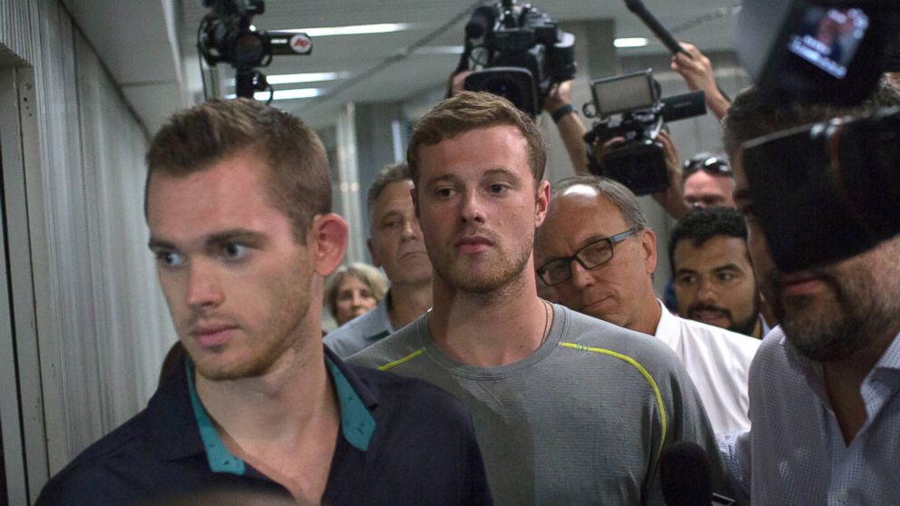 Journalists surround American Olympic swimmers Gunnar Bentz, left, and Jack Conger, center, as they leave the police station at Rio International airport early Thursday Aug. 18, 2016. 