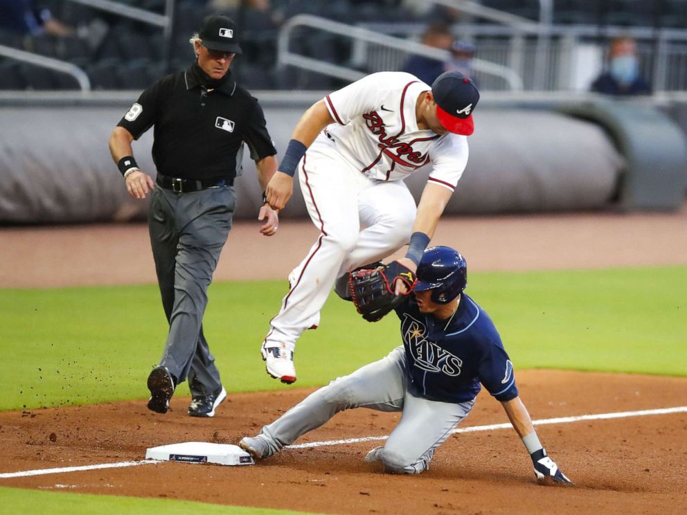 PHOTO: Willy Adames #1 of the Tampa Bay Rays slides under Austin Riley #27 of the Atlanta Braves and rounds third to score on a throwing error in the fifth inning of an MLB game at Truist Park, July 29, 2020, in Atlanta.