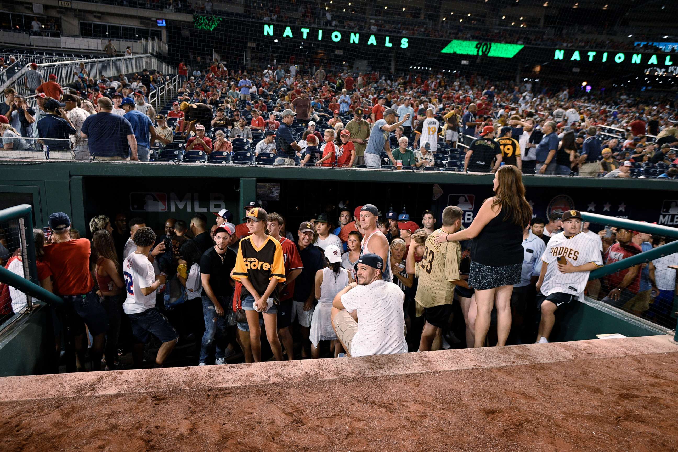 PHOTO: Spectators stand in the visiting team dugout during a stoppage in play due to an incident near the ballpark in the sixth inning of a baseball game between the Washington Nationals and the San Diego Padres, Saturday, July 17, 2021, in Washington.